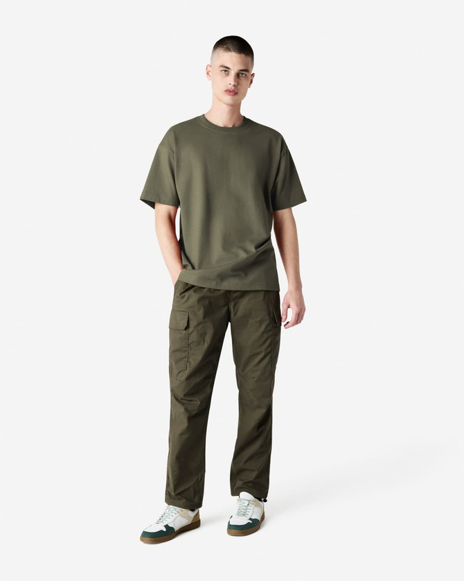 A model wearing an olive green American Apparel Super Heavyweight T-Shirt and matching cargo pants, paired with white sneakers.