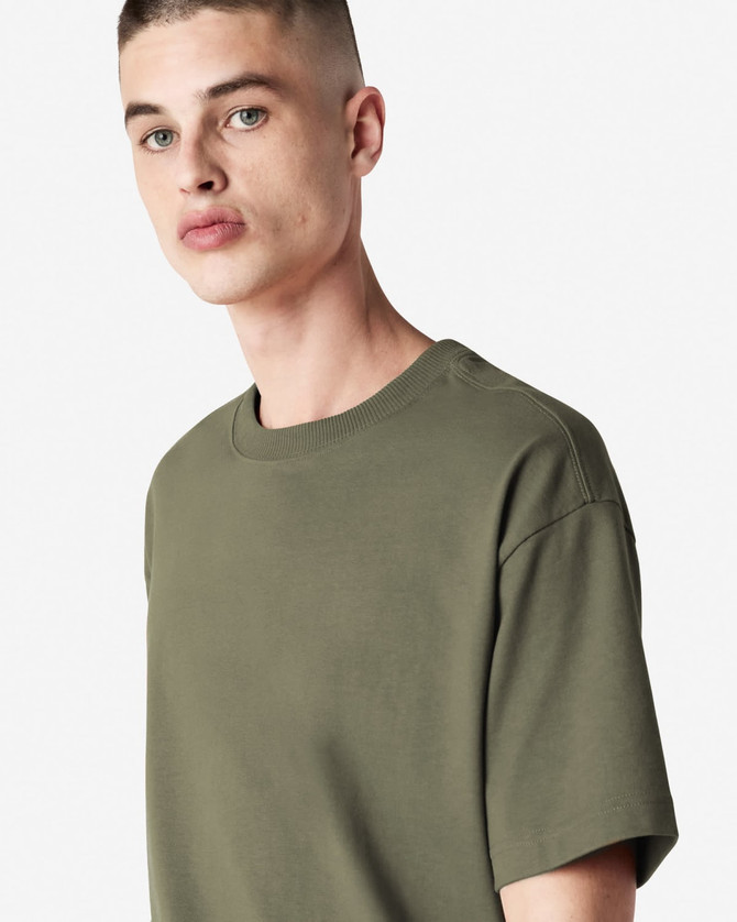 A model wearing an olive green American Apparel Super Heavyweight T-Shirt, featuring a simple design and crew neck.