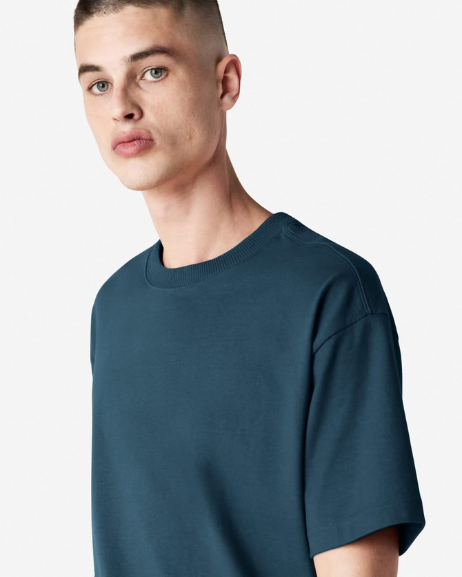 A model wearing a teal American Apparel Super Heavyweight T-Shirt, featuring a round neckline and short sleeves.