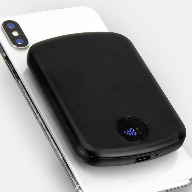 A black wireless charging power bank rests on a smartphone, featuring a digital display and a charging port.