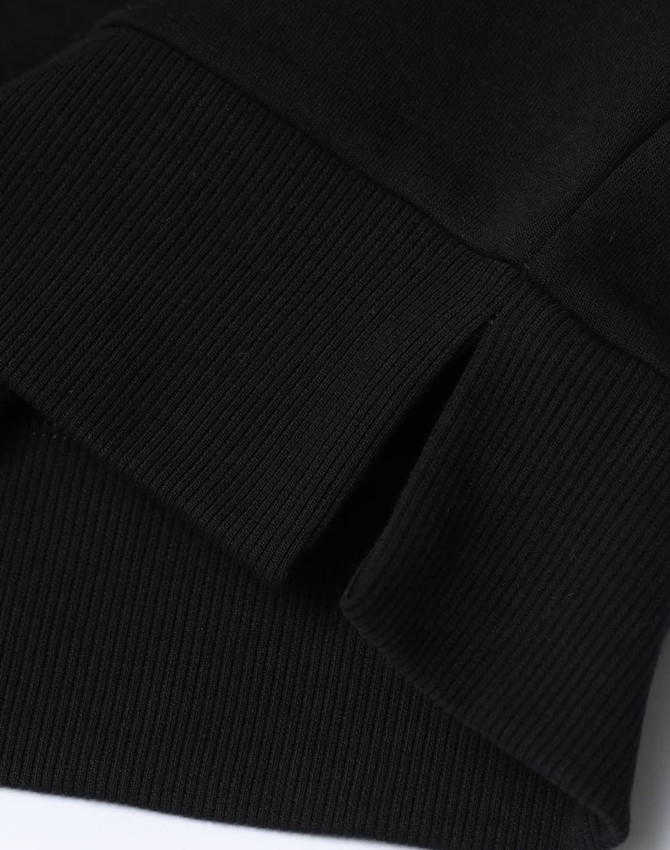 A close-up of the hem and cuff of a black unisex crew neck sweater, featuring a ribbed design and a small split detail.