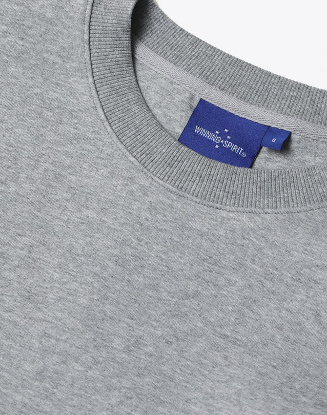 A grey unisex crew neck sweater features a ribbed neckline and a label with branding.