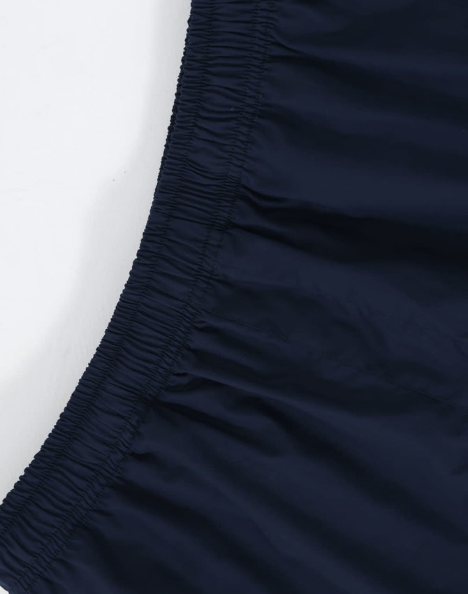 A close-up of unisex mercerised cotton shorts in navy, featuring an elastic waistband. The image includes branding.