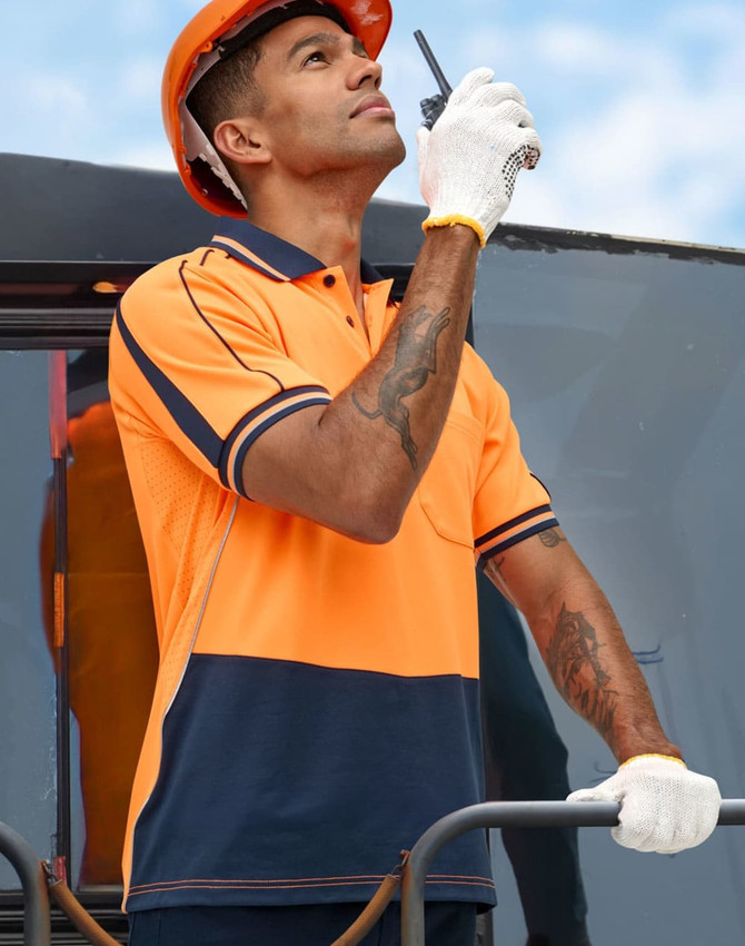 Hi-vis orange and navy sustainable polo shirt on a model wearing a hard hat and gloves, holding a radio.
