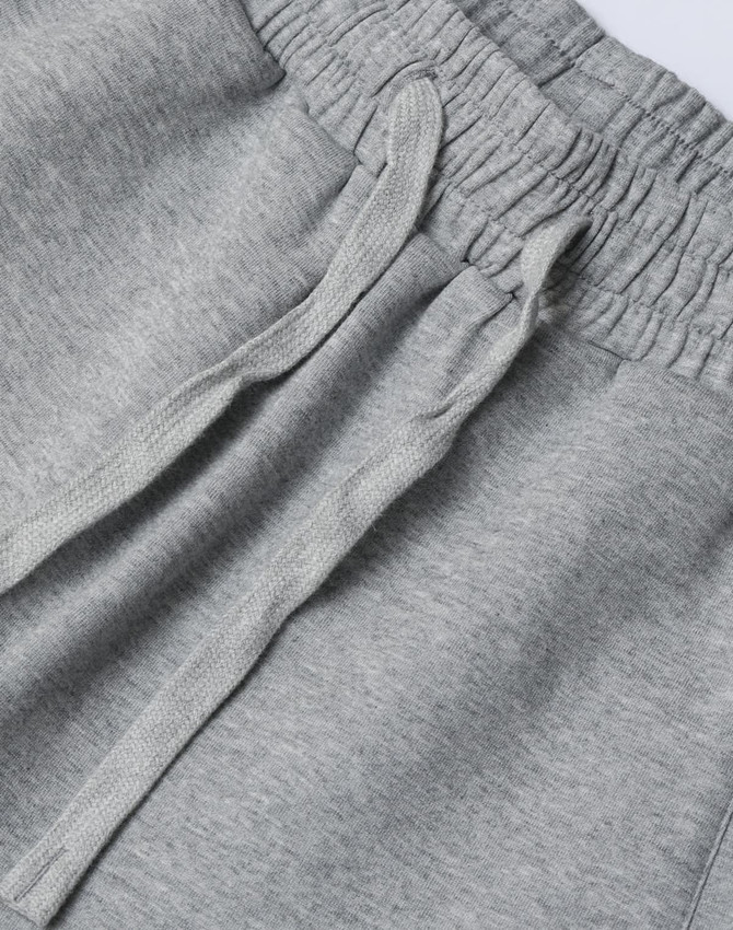 A close-up of grey unisex sweatpants with an elastic waistband and drawstring detail. The fabric appears soft and comfortable.