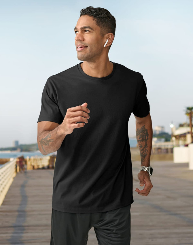 A man in a black short-sleeve tee shirt jogs along a seaside promenade, wearing earbuds and a watch.