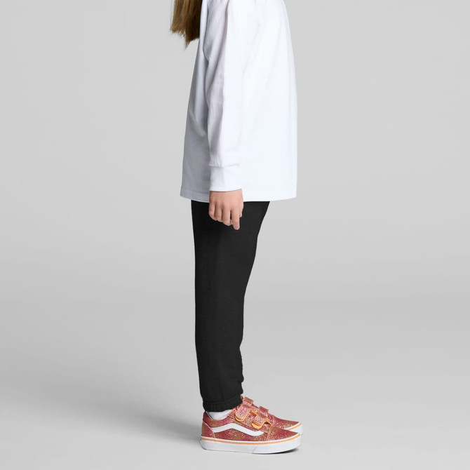 A child wearing black track pants with a white long-sleeve top and pink patterned shoes, standing sideways.