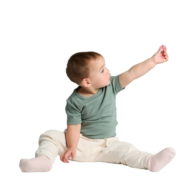 A seated infant wearing a green organic t-shirt and light-coloured trousers, reaching out with one hand.