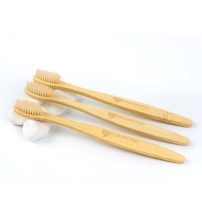 Three bamboo toothbrushes with light brown bristles, placed on smooth white stones. The handles feature a logo.