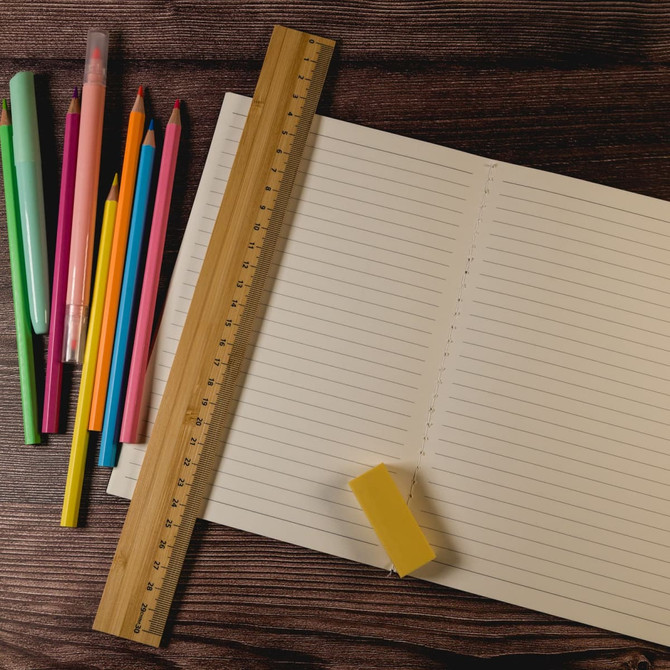 A bamboo 30cm ruler rests on lined paper, accompanied by colourful pens and a yellow eraser.
