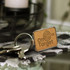 A rectangular wooden key ring with a metal frame, featuring a logo design, attached to several keys.