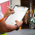 A black clipboard held by a person, featuring a form for listing items, with a forklift in the background.