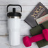 A drink bottle in white with a black lid, alongside a book and a pink dumbbell on a wooden surface.