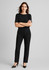 A woman wears black comfort wool stretch relaxed pants paired with a black top and high heels, standing confidently.