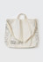 A beige unisex tote bag featuring a repeat pattern of various items and a logo. It has short handles and a long strap.