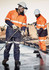 Two men wearing high-visibility orange and navy workwear, including helmets, clean a surface with pressure washers.