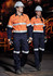 Two individuals wearing orange and navy safety shirts and pants, equipped with hard hats and gloves, in an industrial setting.