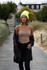 A woman wearing a neon yellow beanie and a beige tank top walks along a wooden path surrounded by greenery.