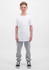 A child stands upright, wearing a plain white t-shirt and grey track pants, with black and white sneakers.