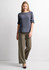 A woman wearing a grey top and olive green soft stretch pants, standing against a light background.