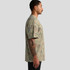 A side view of a man wearing a heavy faded camo T-shirt in various shades of green and brown. The shirt has a logo.