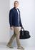 A navy long sleeve shirt worn by a man carrying a black duffle bag, complemented by beige pants and sneakers.