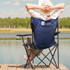 A blue folding chair with armrests, featuring a logo, set against a lakeside backdrop.