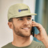 A green cap featuring a logo, worn by a man talking on a phone, smiling.
