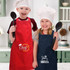 Two children wearing red and navy aprons, each holding a spatula, with chef hats in a kitchen setting.