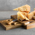 A rectangular cheese board in natural wood with a cheese knife and chunks of cheese on top.