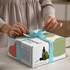 A white die cut box with a locking lid, featuring a colourful design and a light blue ribbon on top.