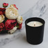 A large black glass candle with a white wax interior, placed beside a bouquet of red and cream roses.