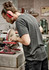 A man wearing a grey T-shirt works on a machine in a workshop, with safety glasses and earmuffs.