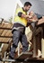 A man in high-visibility clothing uses a nail gun while wearing navy lightweight drill cargo pants on a construction site.