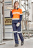 A woman wearing orange and navy workwear, featuring a utility shirt and pants, stands on a construction site holding timber.