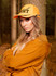 A cap featuring a bright orange visor and camo print inserts, worn by a woman in a forest setting.