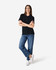 A woman poses in a black Gildan Softstyle Ladies' Double Pique Polo, paired with blue jeans and white sneakers.