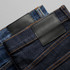 Two pairs of jeans in blue and dark denim, featuring leather patches and contrasting stitching.