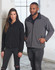 A black and grey softshell jacket worn by a woman and a man, featuring a zip closure and a logo.