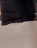 A black heavy quilted puffer jacket featuring a cinched hem and a smooth fabric texture. It has a logo visible.
