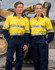 Two individuals wearing bright yellow long-sleeve shirts with reflective tape and navy pants, standing in an industrial setting.