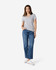 A woman stands wearing a grey Gildan Softstyle ladies' v-neck t-shirt and blue jeans, paired with white sneakers.