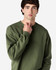 A model wearing an olive green Gildan Softstyle adult sweatshirt. The sweatshirt has a round neckline and long sleeves.