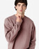 A model wearing a soft pink Gildan Softstyle adult sweatshirt. The sweatshirt features a classic fit and has a logo.