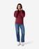 A woman is wearing a burgundy hooded sweatshirt paired with blue jeans and white sneakers. The sweatshirt has a logo.