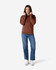 A woman wearing a brown Gildan Softstyle Adult Hooded Sweatshirt and blue jeans, standing against a plain background.