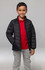 A child wearing a black insulated jacket over a red polo shirt, paired with grey pants. The jacket features a logo.