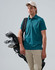 A man wearing a teal polo shirt holds a golf bag with clubs, dressed in light trousers and a cap.