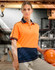 A woman poses wearing a hi-vis orange and navy polo shirt, holding a baseball bat and safety helmet.