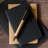 A cardboard pen lies atop two notebooks, one brown and one black, showcasing a sleek and eco-friendly design.